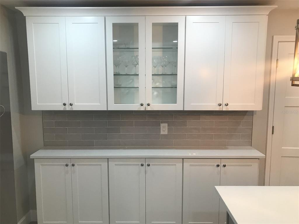 A kitchen featuring white shaker cabinets, a glass-front display cabinet, and a gray subway tile backsplash — 2369 19TH AVENUE SW UNIT B, LARGO, FL