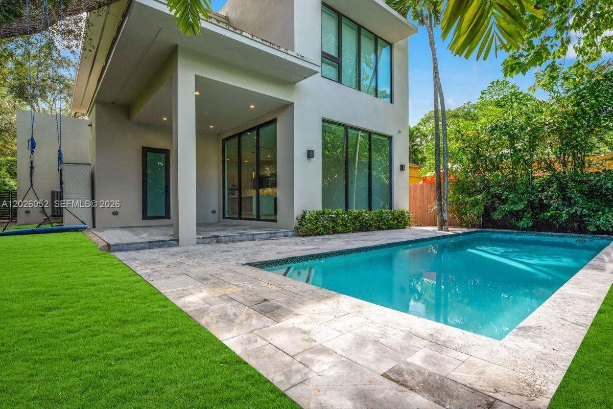 A modern two-story house features a backyard swimming pool, stone patio, and artificial grass lawn — 3741 Kumquat Ave, Miami FL 33133, MIAMI, FL
