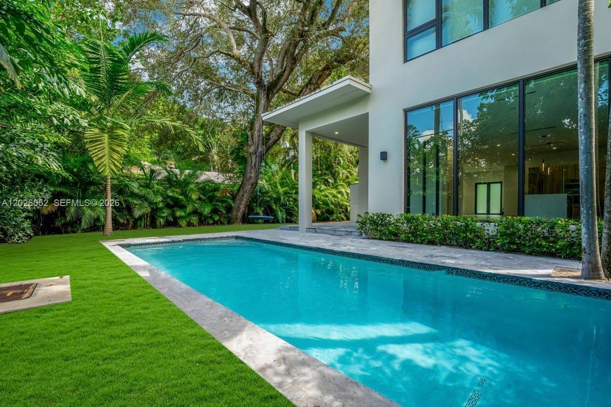 A modern house exterior features a rectangular swimming pool, a lawn, and lush landscaping — 3741 Kumquat Ave, Miami FL 33133, MIAMI, FL