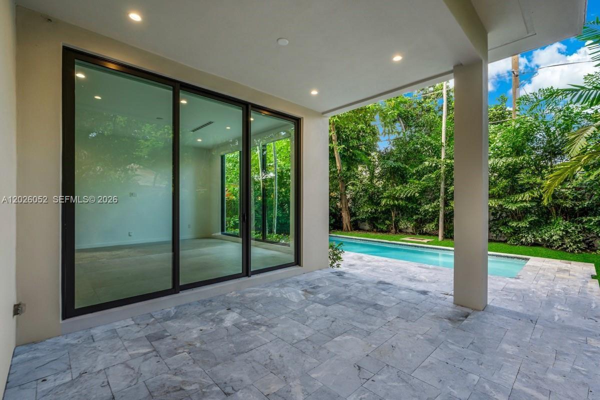 A covered stone patio overlooks a swimming pool surrounded by lush green trees — 3741 Kumquat Ave, Miami FL 33133, MIAMI, FL
