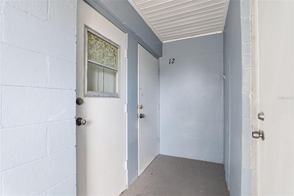 This exterior view shows a covered entryway with three white doors and unit number 12 — 302 LINCOLN AVENUE UNIT 12, CAPE CANAVERAL, FL