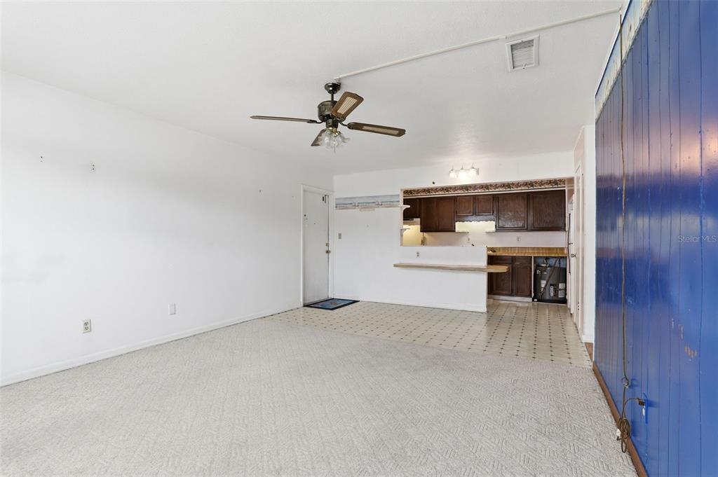 A living room with carpeted flooring, a ceiling fan, and an open kitchen with dark cabinets — 302 LINCOLN AVENUE UNIT 12, CAPE CANAVERAL, FL