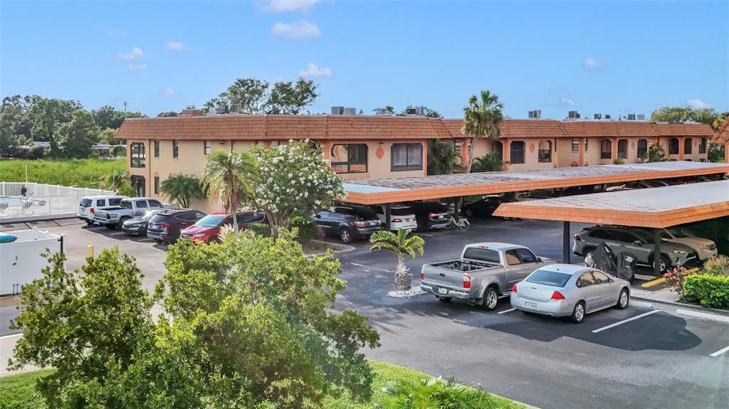 An apartment building exterior with a parking lot featuring covered carports and several parked vehicles — 10192 SEMINOLE ISLAND DRIVE UNIT 10192, LARGO, FL