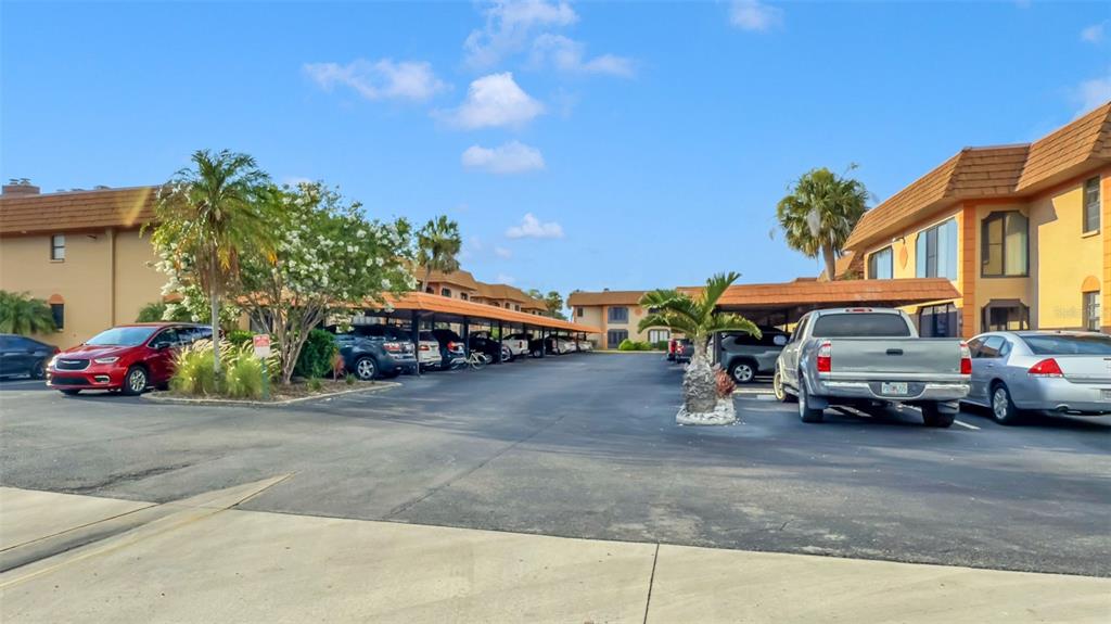 A parking lot with covered spaces sits between two-story apartment buildings under a blue sky — 10192 SEMINOLE ISLAND DRIVE UNIT 10192, LARGO, FL