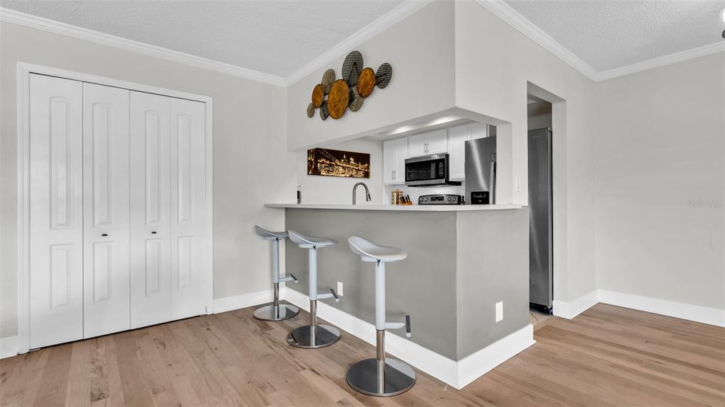 A kitchen breakfast bar with three stools faces a dining area with wood flooring — 10192 SEMINOLE ISLAND DRIVE UNIT 10192, LARGO, FL