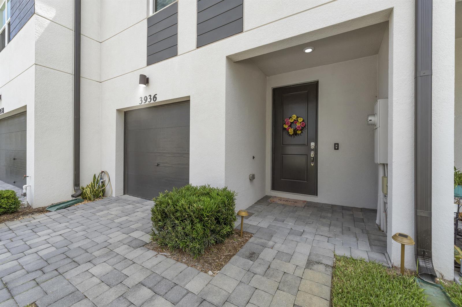 A modern townhouse exterior features a dark garage door, a front door with a wreath, and pavers — 3936 SE Caladium Court # 3936, Stuart FL 34997, STUART, FL