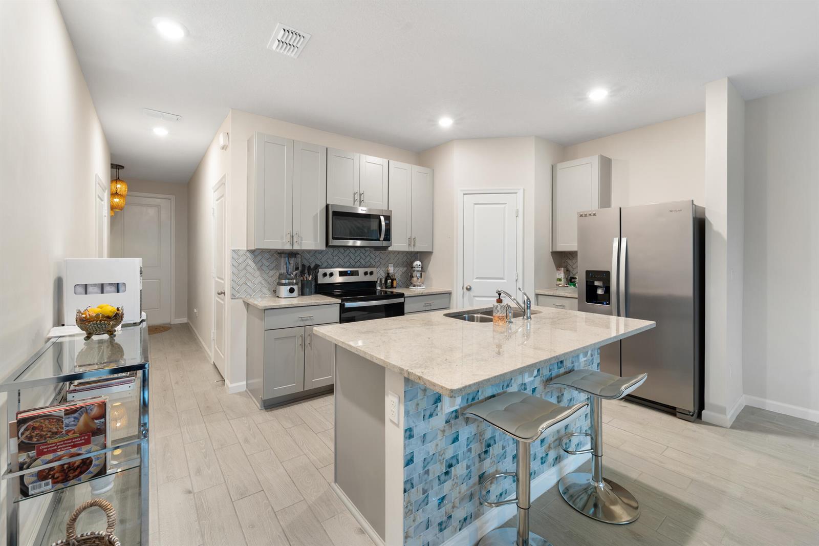 A kitchen features gray cabinets, stainless steel appliances, a granite island, and blue tile accents — 3936 SE Caladium Court # 3936, Stuart FL 34997, STUART, FL