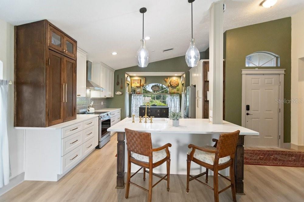 A kitchen features white cabinetry, a large island with bar stools, and olive green walls — 10551 MAGRATH LANE, NEW PORT RICHEY, FL