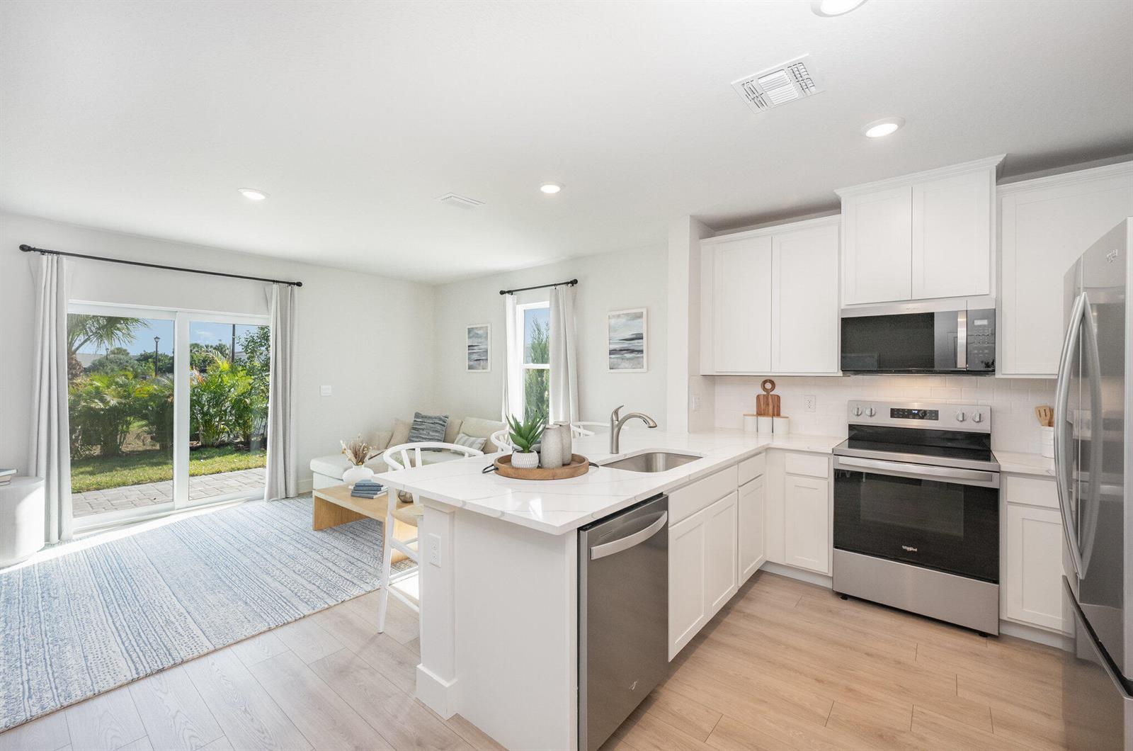 A modern kitchen with white cabinets and stainless steel appliances opens to a living area — 8128 Cobblestone Drive, Fort Pierce FL 34945, FORT PIERCE, FL
