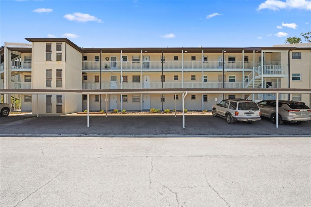A three-story apartment building with exterior walkways and a covered parking area in front — 5245 AMULET DRIVE UNIT 306, NEW PORT RICHEY, FL