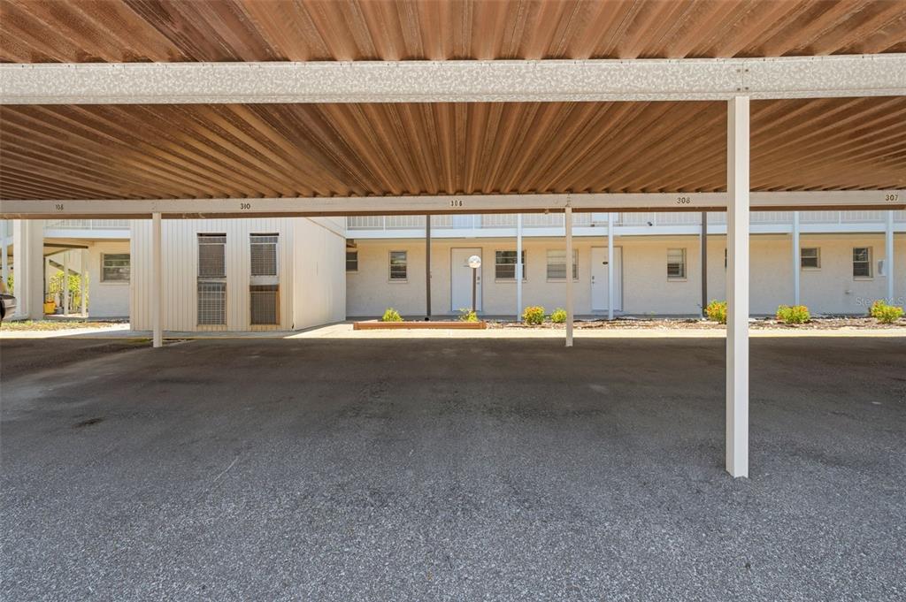 A covered parking area sits in front of a multi-story apartment building with numbered units — 5245 AMULET DRIVE UNIT 306, NEW PORT RICHEY, FL