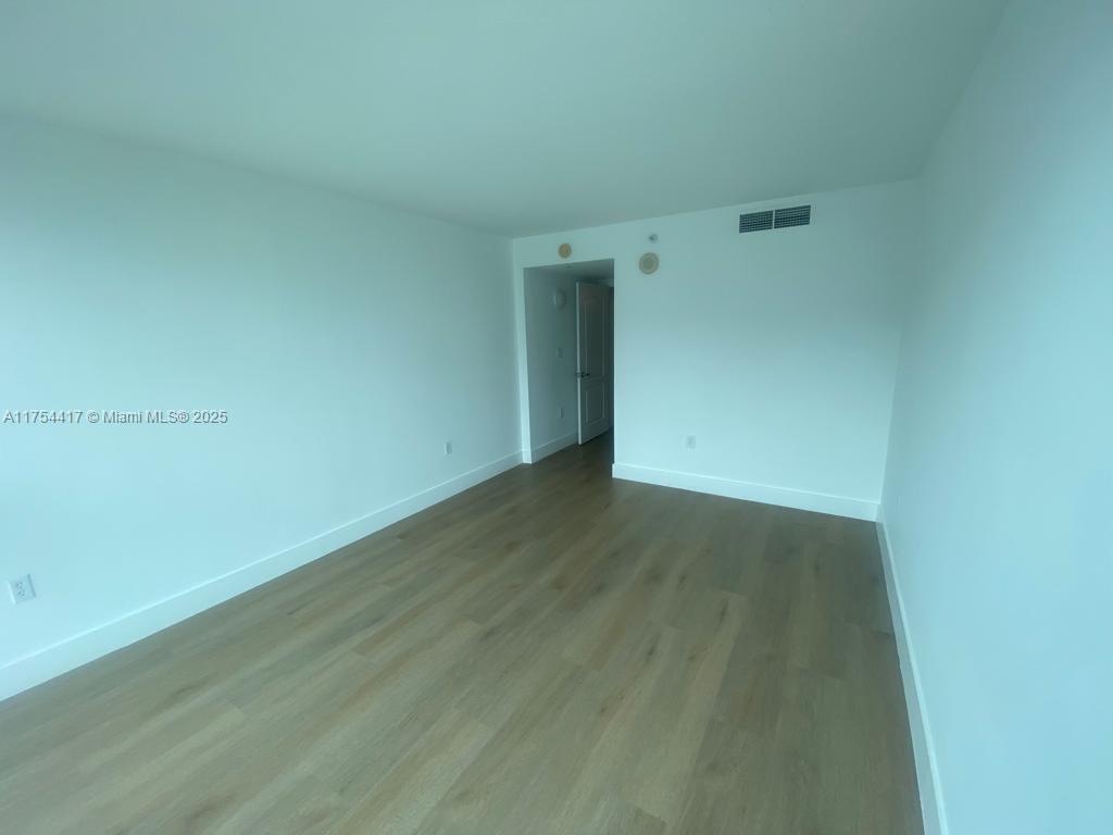 An empty room features white walls, light wood-look flooring, and a doorway leading to another area — 2101 Brickell Ave # 1401, Miami FL 33129, MIAMI, FL