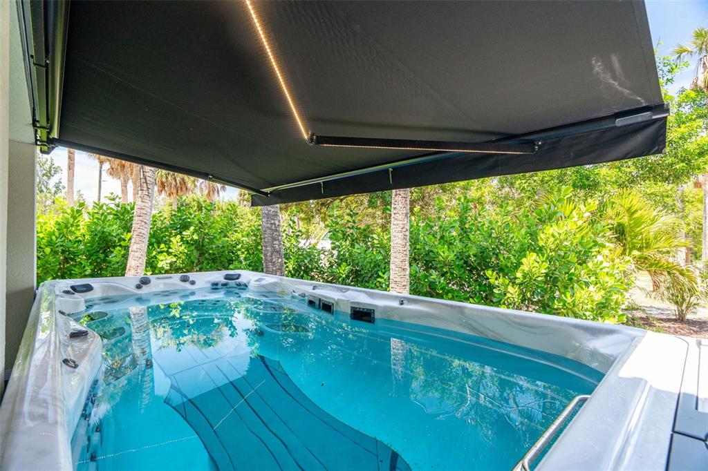 A swim spa sits on a patio under a retractable awning with integrated lighting — 4817 LIMESTONE DRIVE, PORT RICHEY, FL