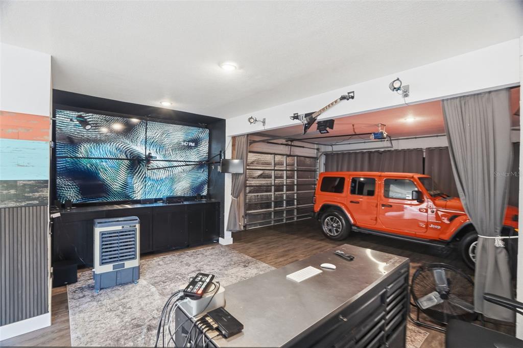 A garage converted into a living space with a large wall-mounted screen and parked Jeep — 4817 LIMESTONE DRIVE, PORT RICHEY, FL