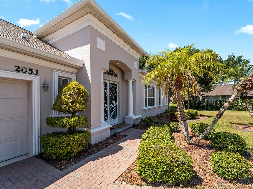 The exterior of a beige house features a brick walkway, a palm tree, and landscaping — 2053 MATTAMY CT, VENICE, FL