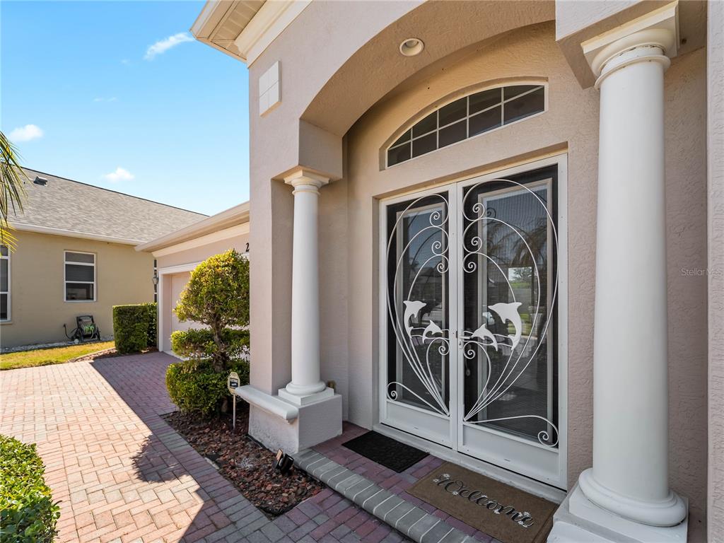 The exterior entrance features double glass doors with dolphin designs, white columns, and brick pavers — 2053 MATTAMY CT, VENICE, FL