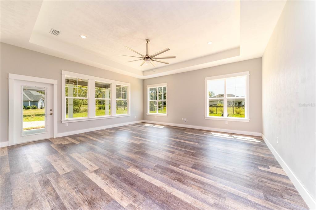 A bright, empty room features wood-look flooring, a tray ceiling with a fan, and large windows — 0 71ST LANE, O'BRIEN, FL