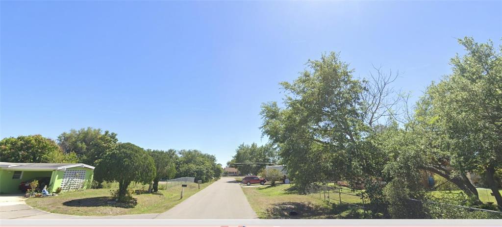 A paved street leads through a residential neighborhood with trees and a green house — 629 GAINES STREET, PORT CHARLOTTE, FL