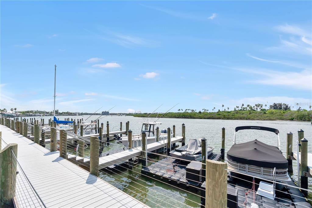 A wooden dock extends over water toward several moored boats under a blue sky — 460 BOUCHELLE DRIVE UNIT 101, NEW SMYRNA BEACH, FL