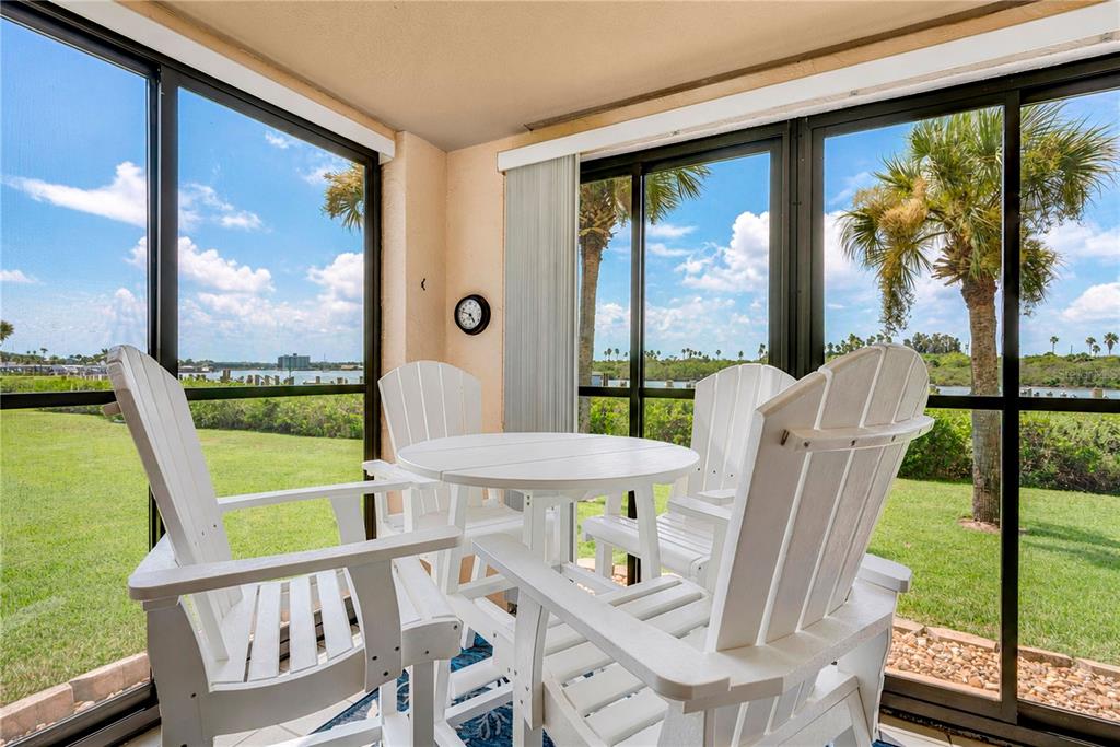 A screened-in porch features white Adirondack chairs, a round table, and views of a waterway — 460 BOUCHELLE DRIVE UNIT 101, NEW SMYRNA BEACH, FL