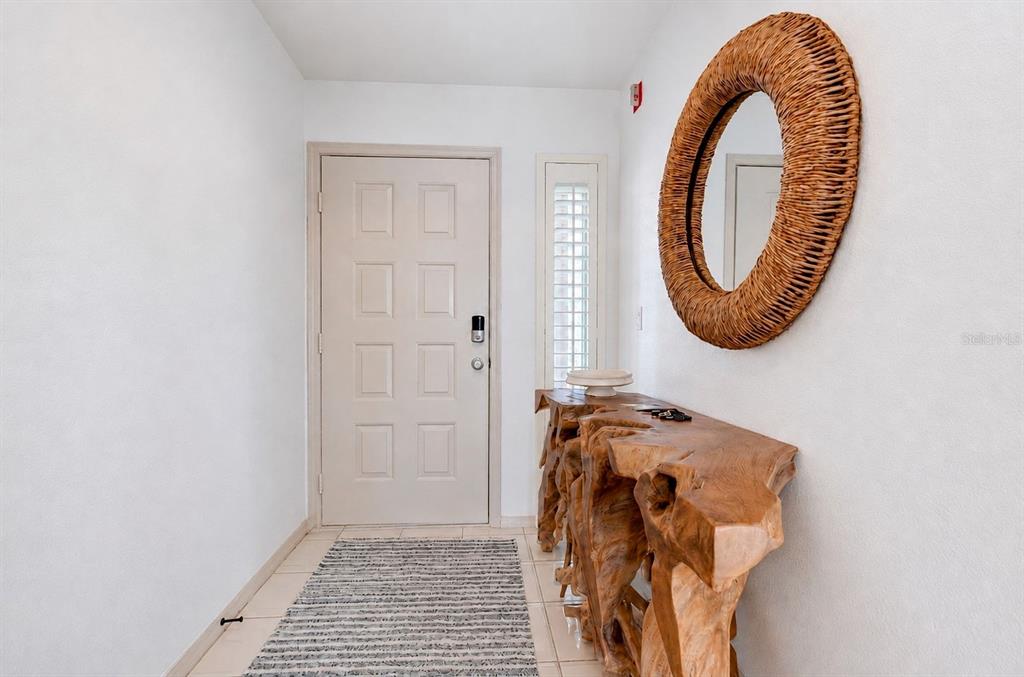 An entryway features a white door, a rustic wooden console table, and a round wicker mirror — 460 BOUCHELLE DRIVE UNIT 101, NEW SMYRNA BEACH, FL