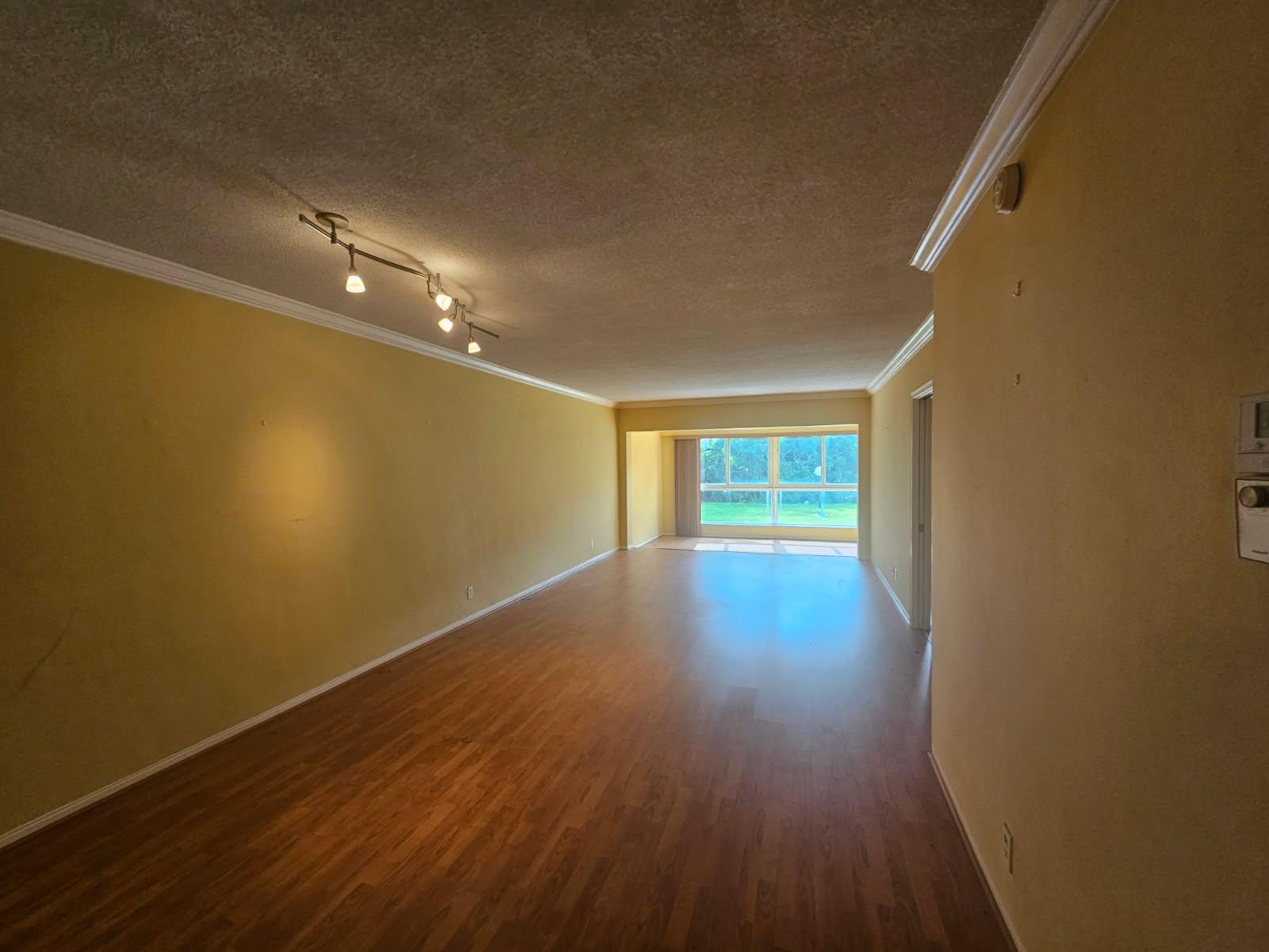 An empty living room with yellow walls, wood-look flooring, and a track lighting fixture — 3401 Spanish Trail # 152, Delray Beach FL 33483, DELRAY BEACH, FL