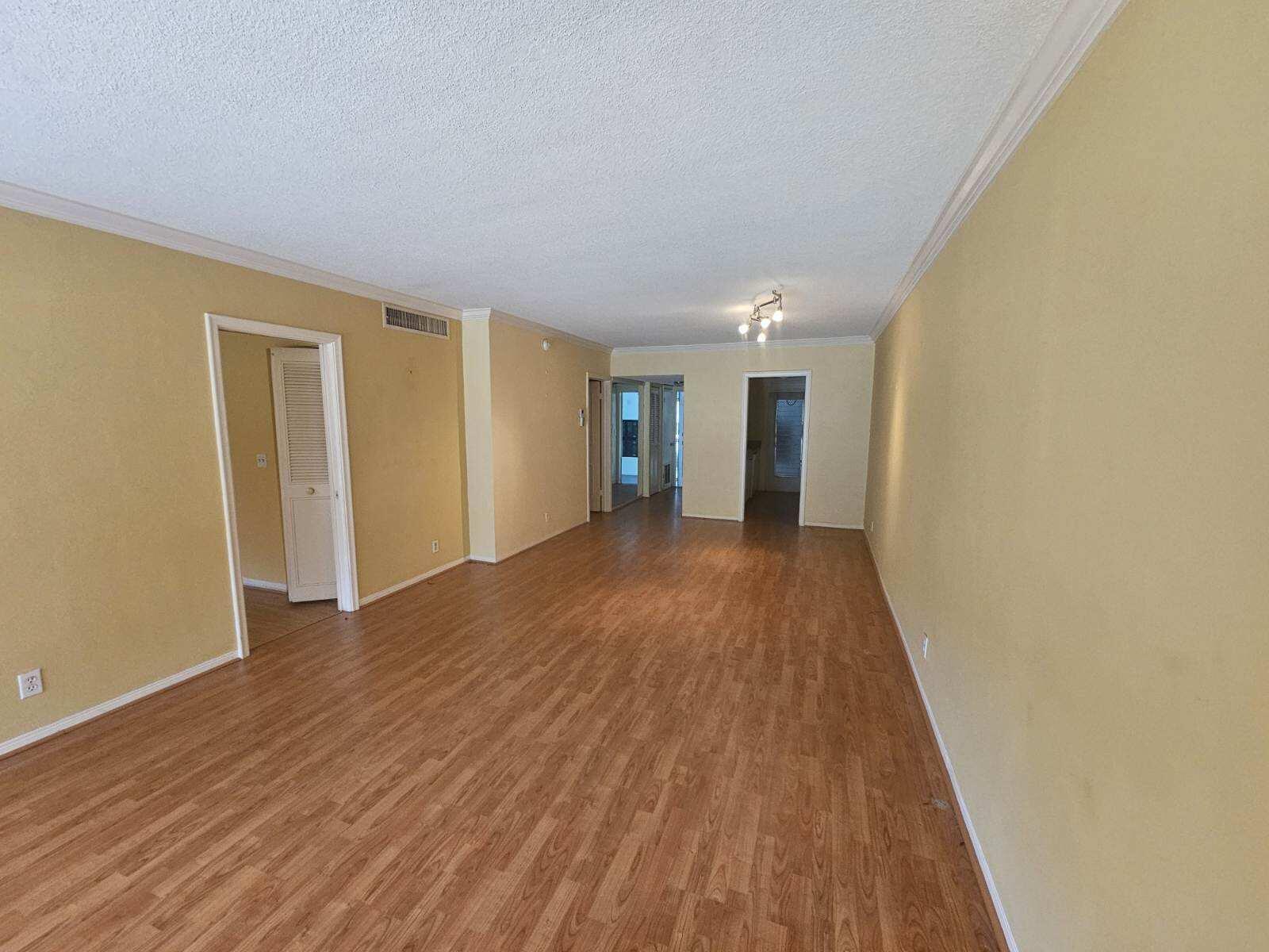 An empty living room features light yellow walls, wood-look flooring, and multiple doorways — 3401 Spanish Trail # 152, Delray Beach FL 33483, DELRAY BEACH, FL
