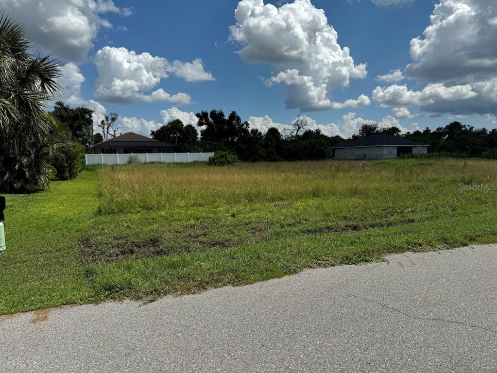 A vacant, grassy residential lot sits next to a paved road under a cloudy sky — 139 SESAME ROAD W, ROTONDA WEST, FL