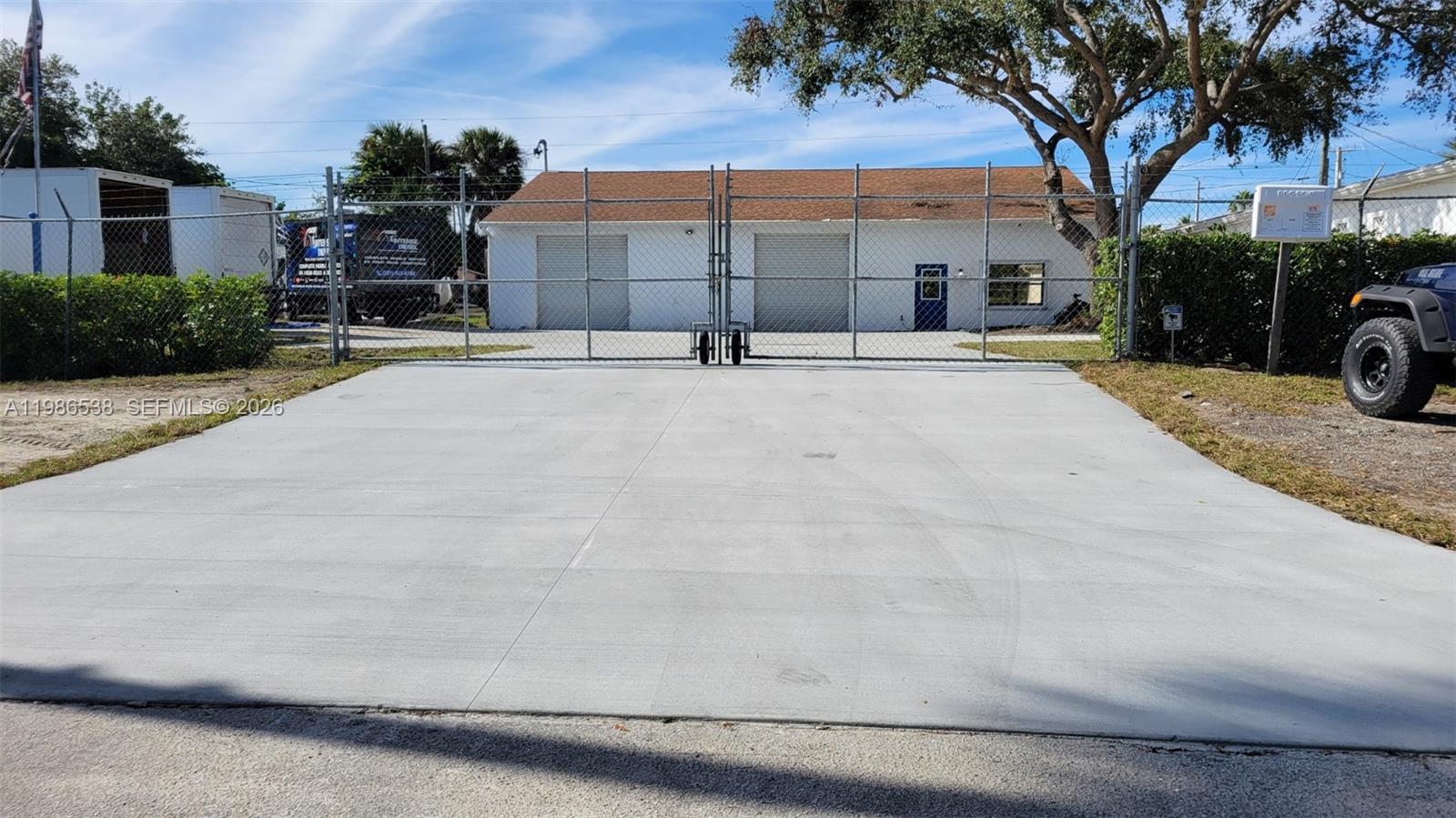 A fenced-in concrete driveway leads to a white building with two garage doors — 645 Old Dixie Hwy, Sebastian FL 32958, SEBASTIAN, FL