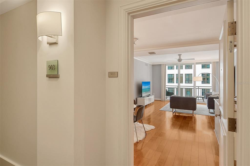 A view from a hallway into a living room with hardwood floors and balcony windows — 1350 MAIN STREET UNIT 903, SARASOTA, FL