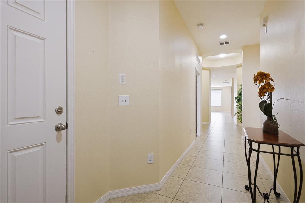 A hallway with beige walls, tiled floors, a white door, and a small console table — 2211 BARRACUDA COURT, HOLIDAY, FL