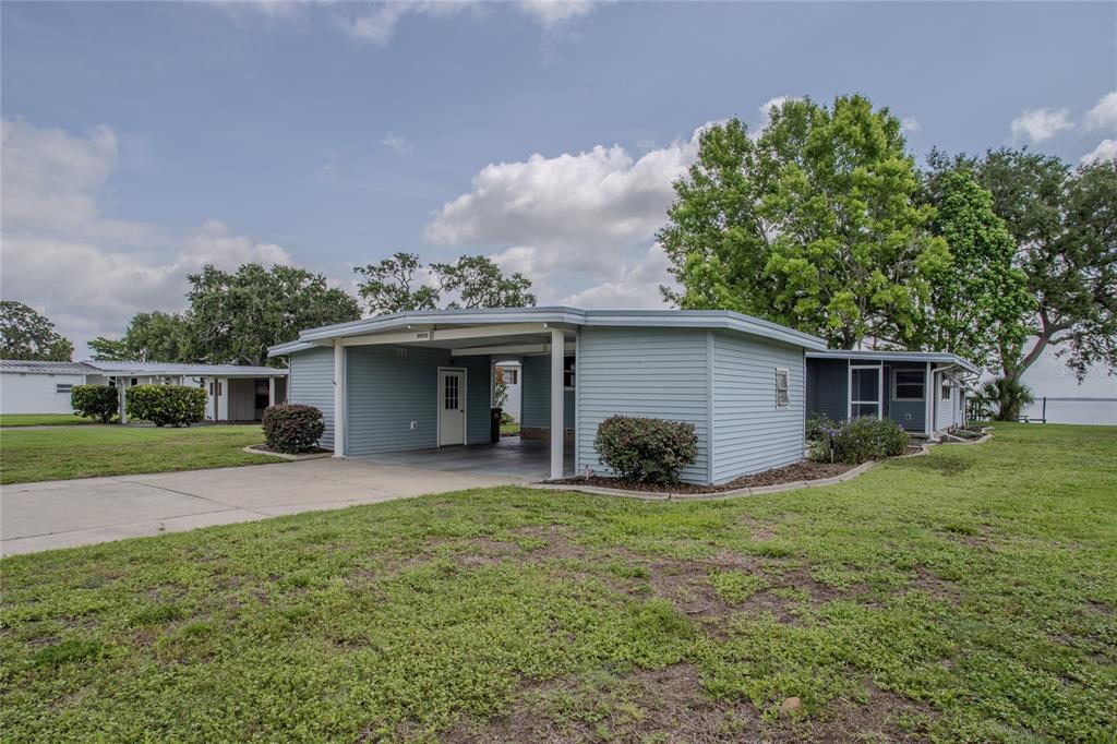 A light blue single-story house features a carport and a large grassy yard — 34232 ISLAND DRIVE, LEESBURG, FL