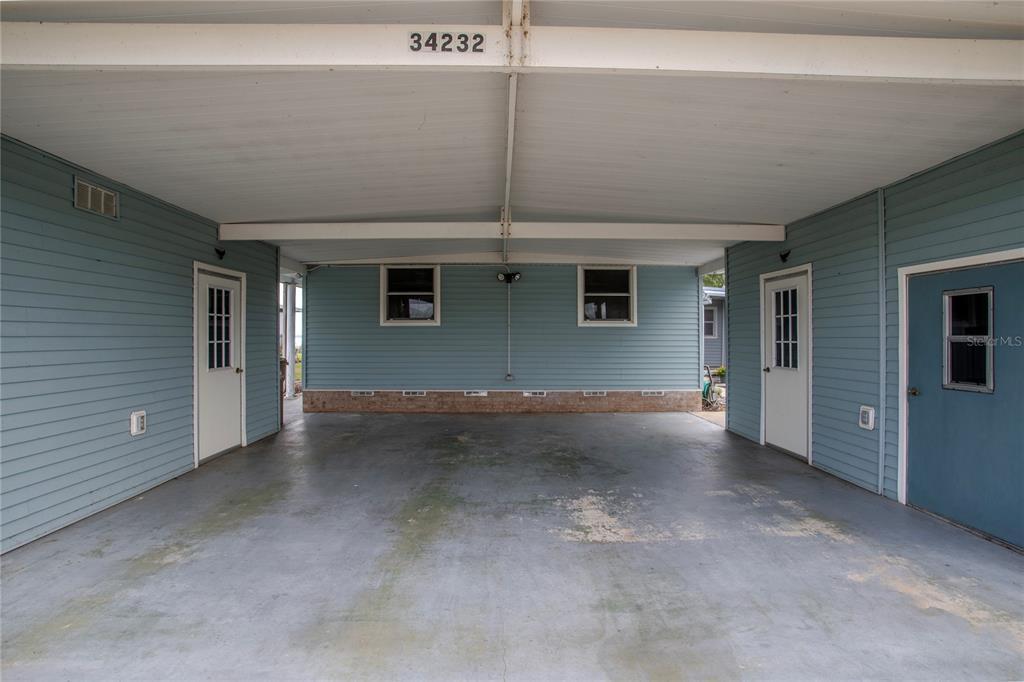 A covered carport with blue siding, concrete flooring, and three exterior doors — 34232 ISLAND DRIVE, LEESBURG, FL