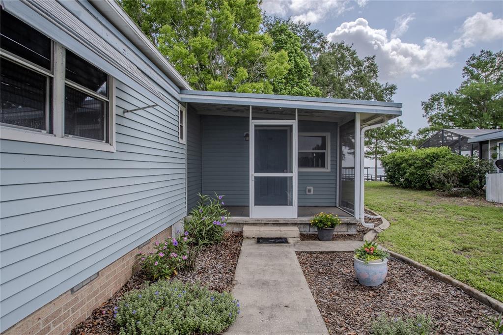 A blue-sided house features a screened-in porch with a concrete walkway and landscaped garden beds — 34232 ISLAND DRIVE, LEESBURG, FL
