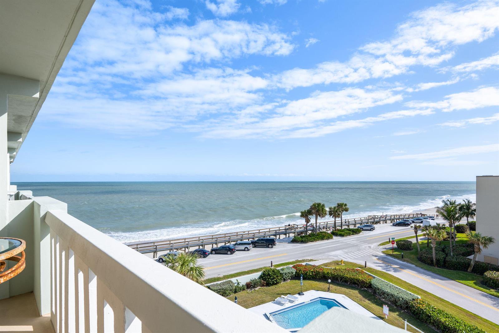 A high-angle view from a balcony overlooking a coastal road, beach, and swimming pool — 4049 Ocean Drive # 505, Vero Beach FL 32963, VERO BEACH, FL