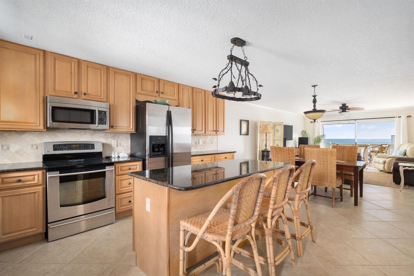 A kitchen with light wood cabinets, black granite countertops, and an island with wicker stools — 4049 Ocean Drive # 505, Vero Beach FL 32963, VERO BEACH, FL