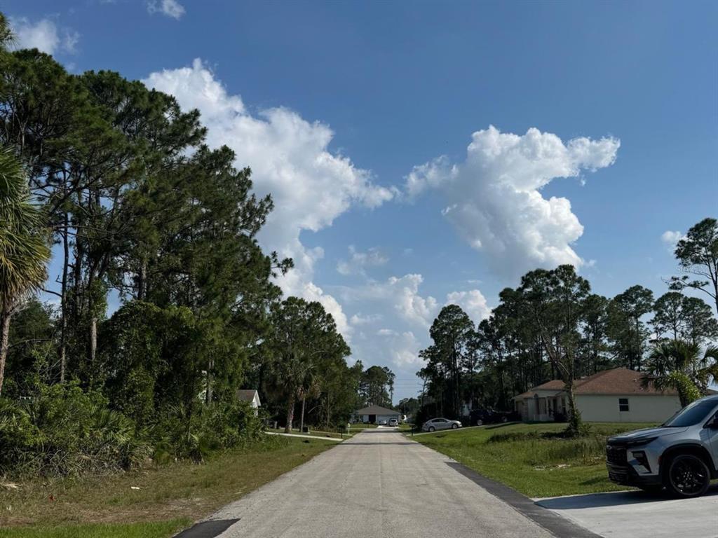 A paved residential street leads toward houses surrounded by trees under a blue, cloudy sky — 762 HARRIET, PALM BAY, FL