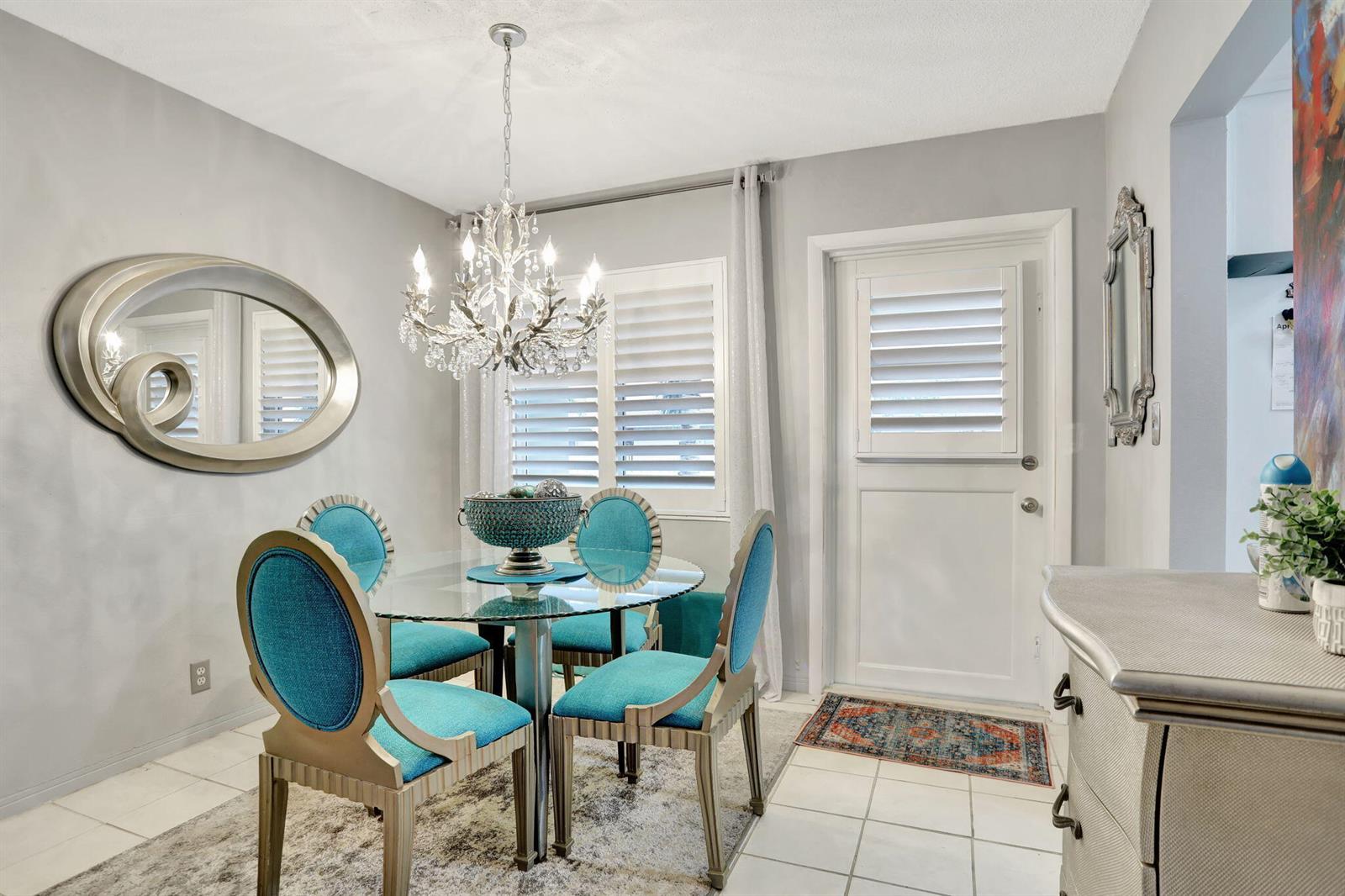 A dining room features a glass table, four teal chairs, a chandelier, and a white door — 2131 NE 42nd Court # 210e, Lighthouse Point FL 33064, LIGHTHOUSE POINT, FL