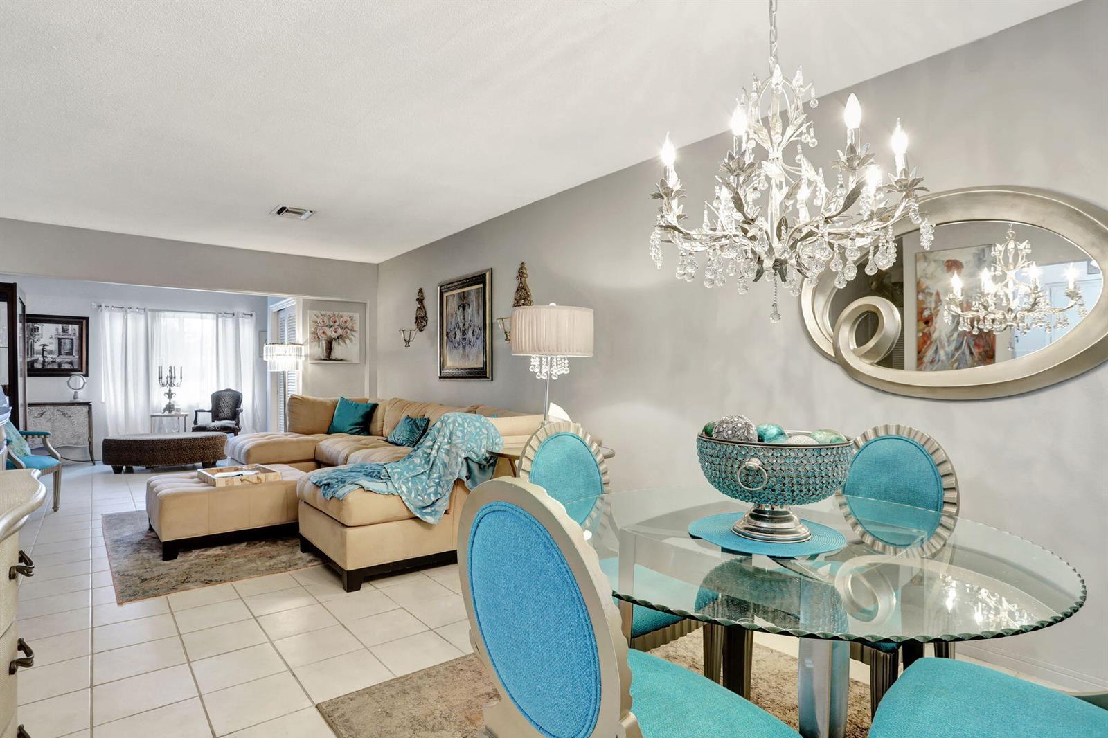 A dining area with a glass table and blue chairs sits beside a living room — 2131 NE 42nd Court # 210e, Lighthouse Point FL 33064, LIGHTHOUSE POINT, FL