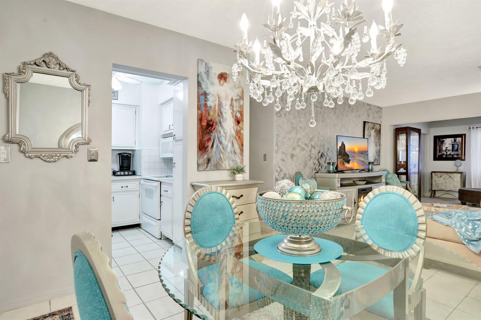 A dining area features a glass table, turquoise chairs, a crystal chandelier, and a mirror — 2131 NE 42nd Court # 210e, Lighthouse Point FL 33064, LIGHTHOUSE POINT, FL