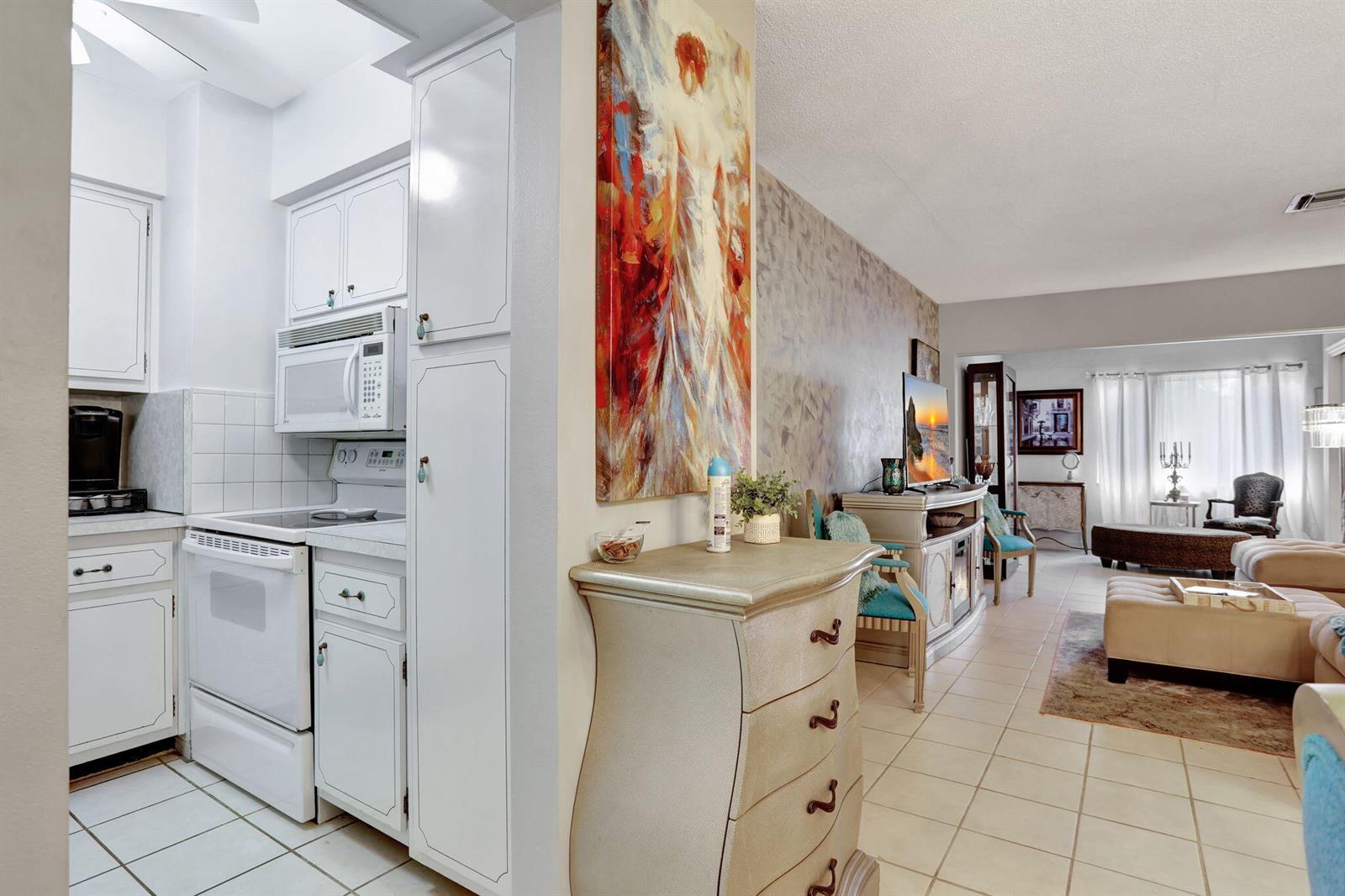 A kitchen with white appliances and cabinets opens into a living area with tile flooring — 2131 NE 42nd Court # 210e, Lighthouse Point FL 33064, LIGHTHOUSE POINT, FL