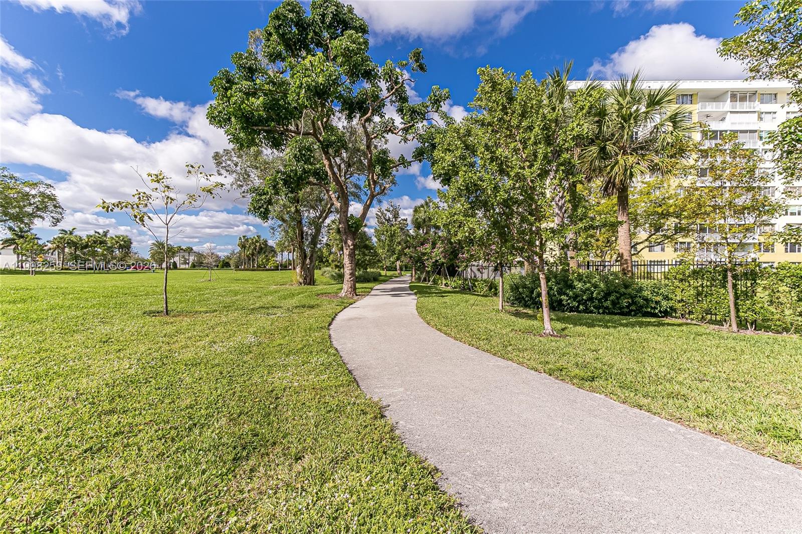 A paved walking path winds through a grassy park area with trees and a building — 4350 Hillcrest Dr # 303, Hollywood FL 33021, HOLLYWOOD, FL