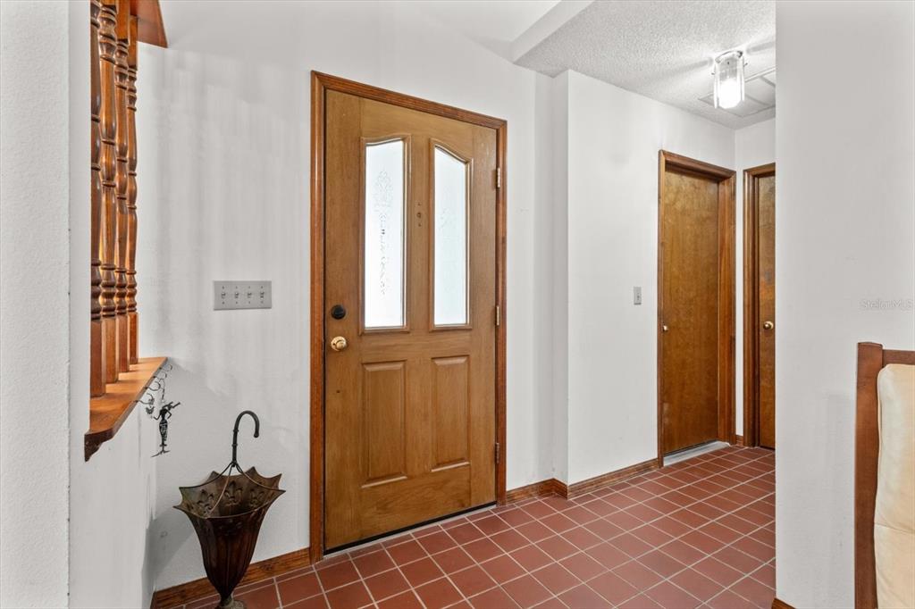 An entryway features a wooden front door, red tile flooring, and a wooden stair railing — 10025 KIMBROUGH DRIVE, BROOKSVILLE, FL