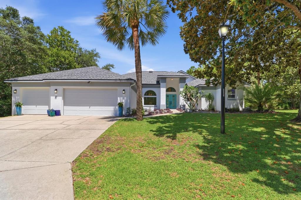 A single-story house with a three-car garage, a palm tree, and a turquoise front door — 21 FIDDLEWOOD COURT, HOMOSASSA, FL