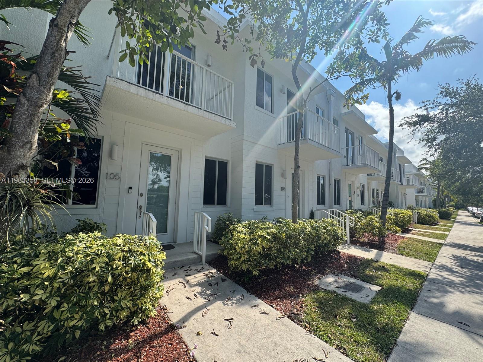 A row of white two-story townhouses features balconies and small front gardens along a sidewalk — 2630 NE 213 St # 105, Miami FL 33180, MIAMI, FL