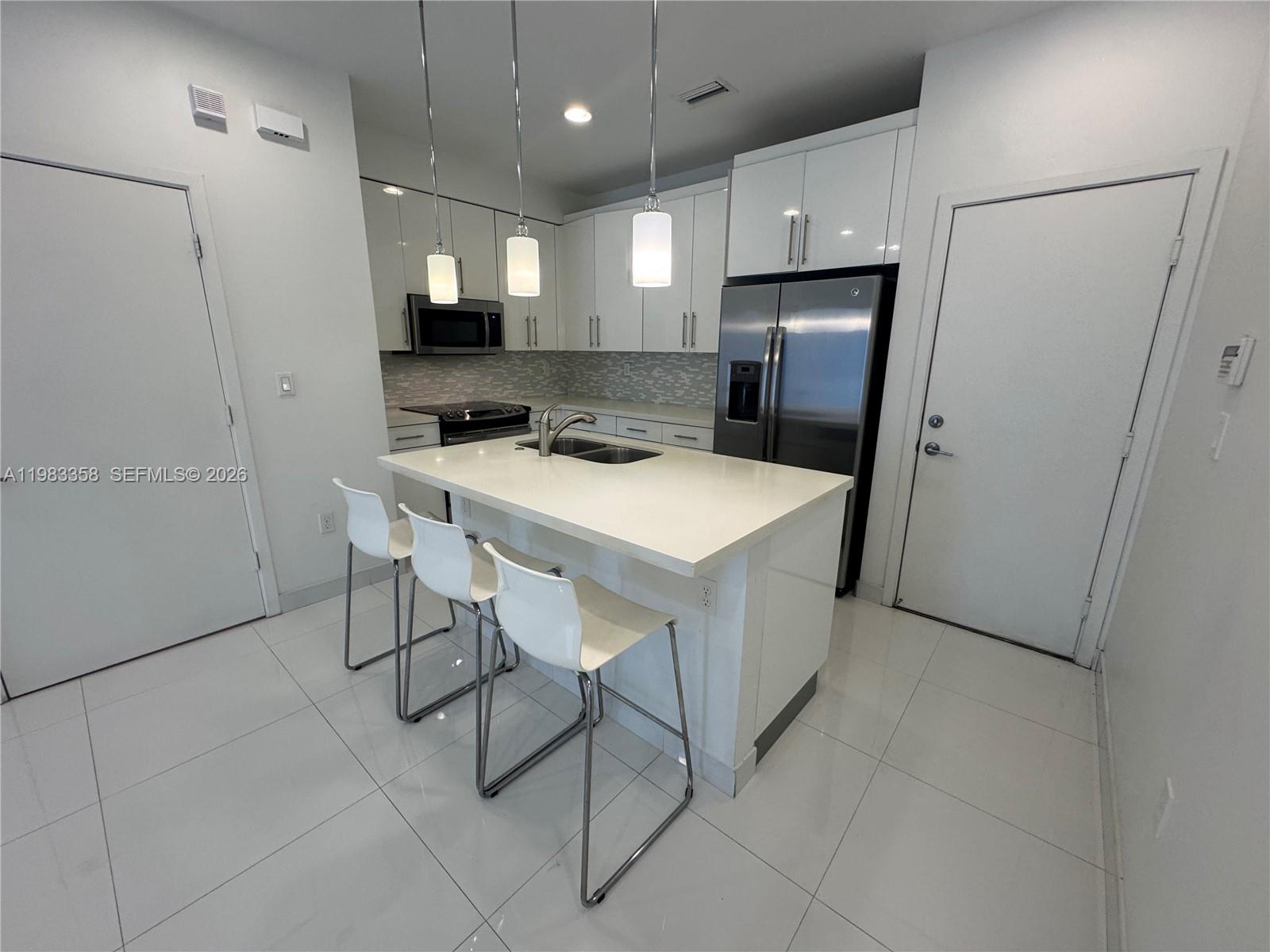 A modern kitchen features white cabinets, stainless steel appliances, a central island, and tile flooring — 2630 NE 213 St # 105, Miami FL 33180, MIAMI, FL