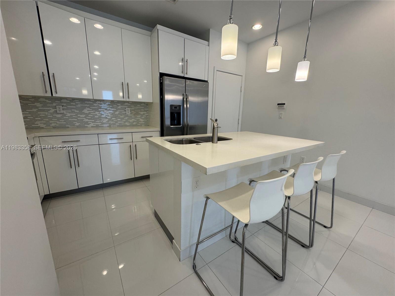 A modern kitchen features white glossy cabinets, stainless steel appliances, and a central island — 2630 NE 213 St # 105, Miami FL 33180, MIAMI, FL