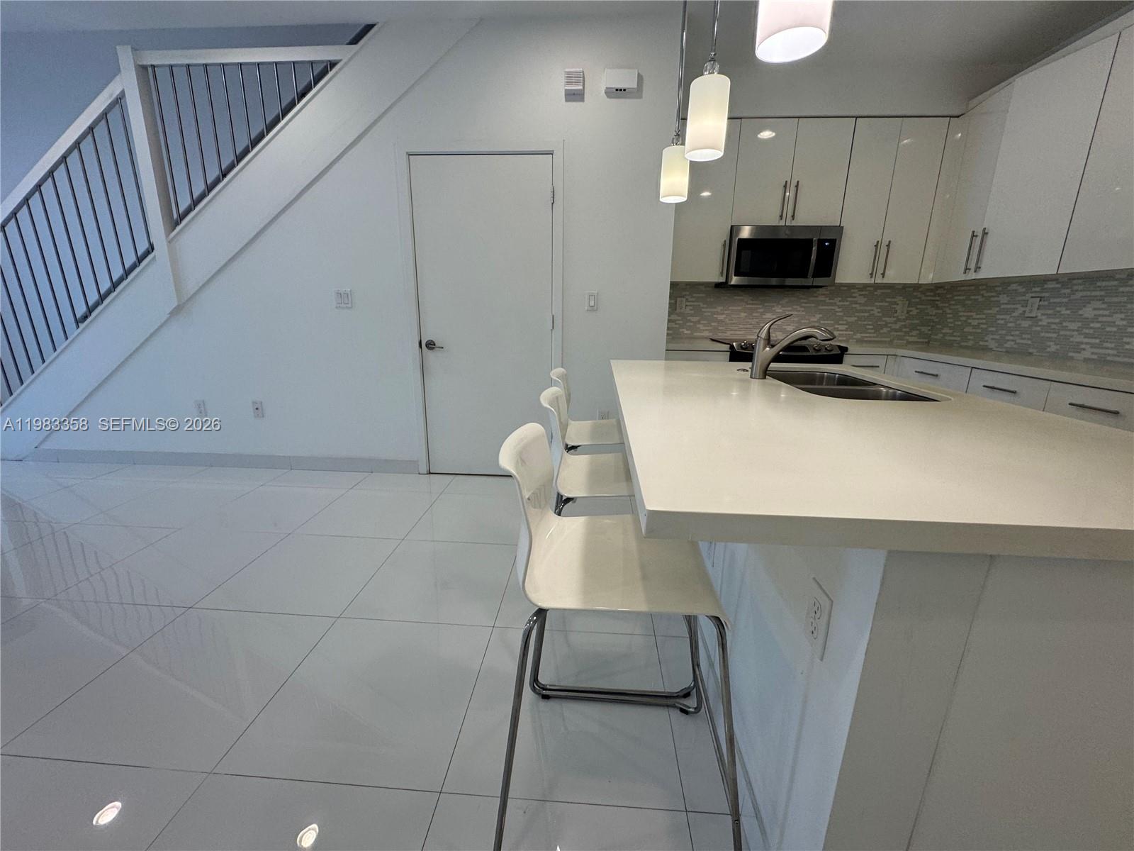 A modern kitchen features white cabinetry, a quartz island with bar seating, and tiled floors — 2630 NE 213 St # 105, Miami FL 33180, MIAMI, FL