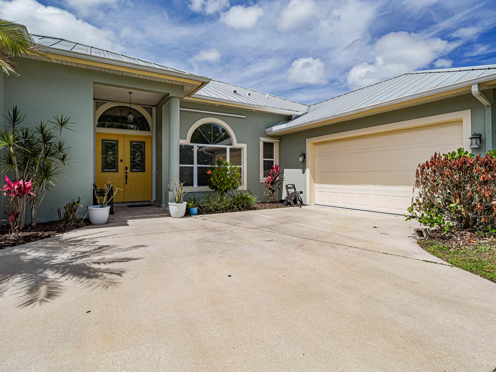 A light green house with a yellow front door, metal roof, and concrete driveway — 6489 53rd Circle, Vero Beach FL 32967, VERO BEACH, FL
