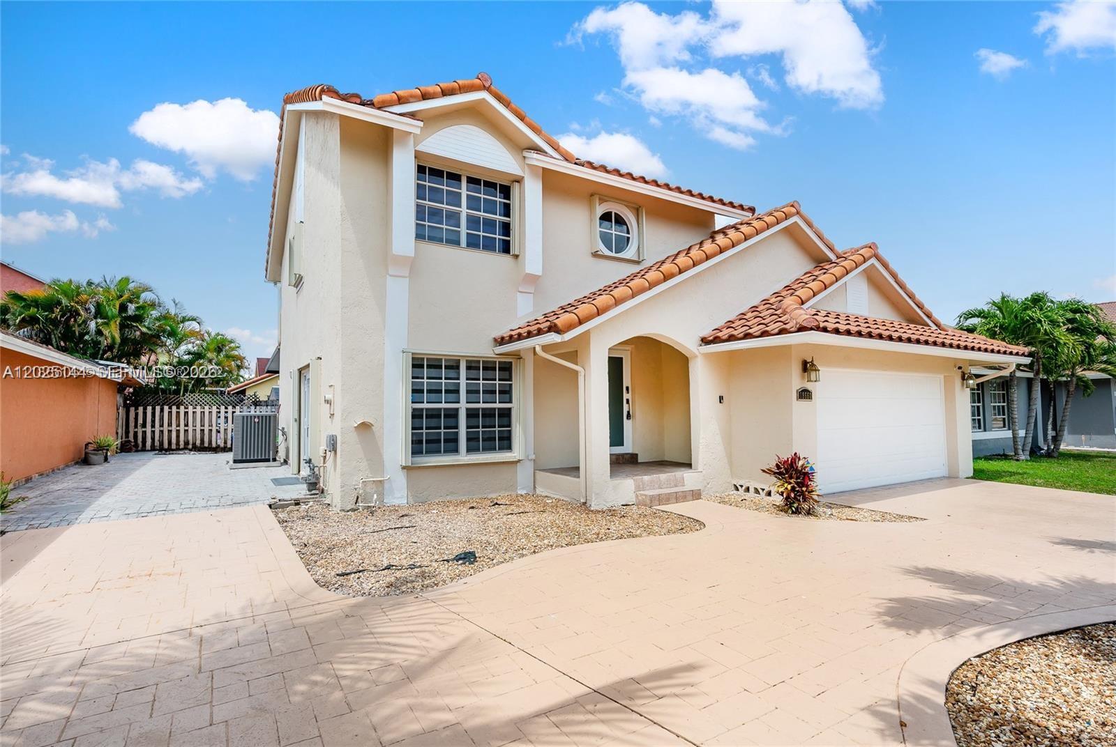 A two-story house with a tan stucco exterior, tile roof, and a paved driveway — 18660 NW 78th Ave # 0, Hialeah FL 33015, HIALEAH, FL